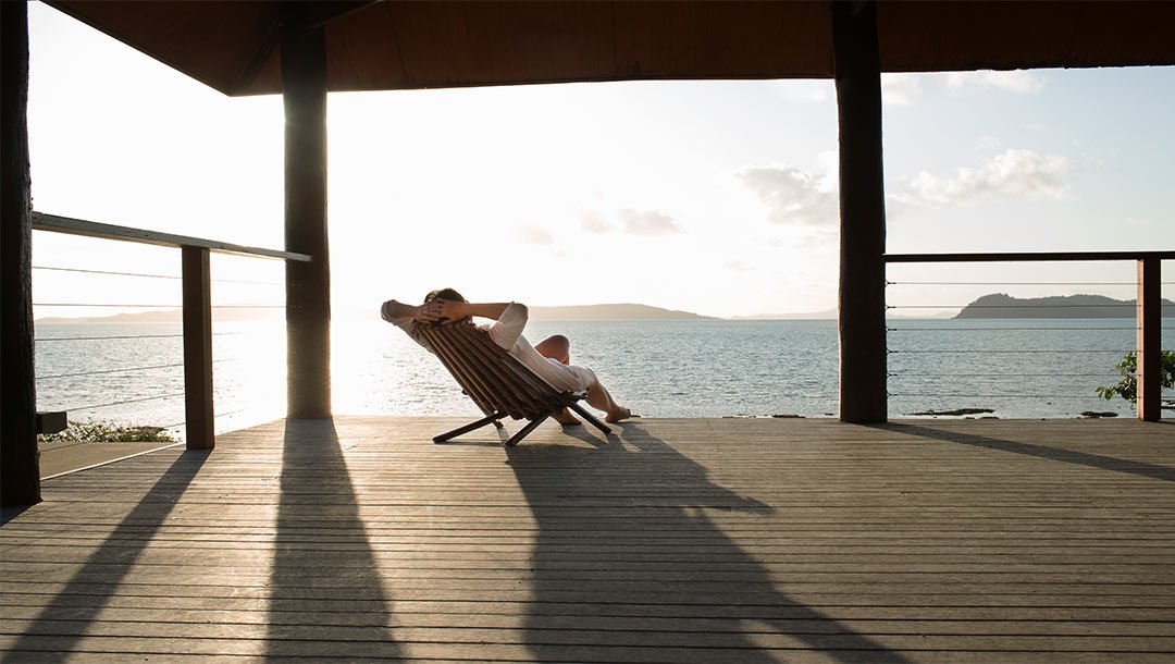 Person relaxing on a deck chair overlooking the ocean at sunset