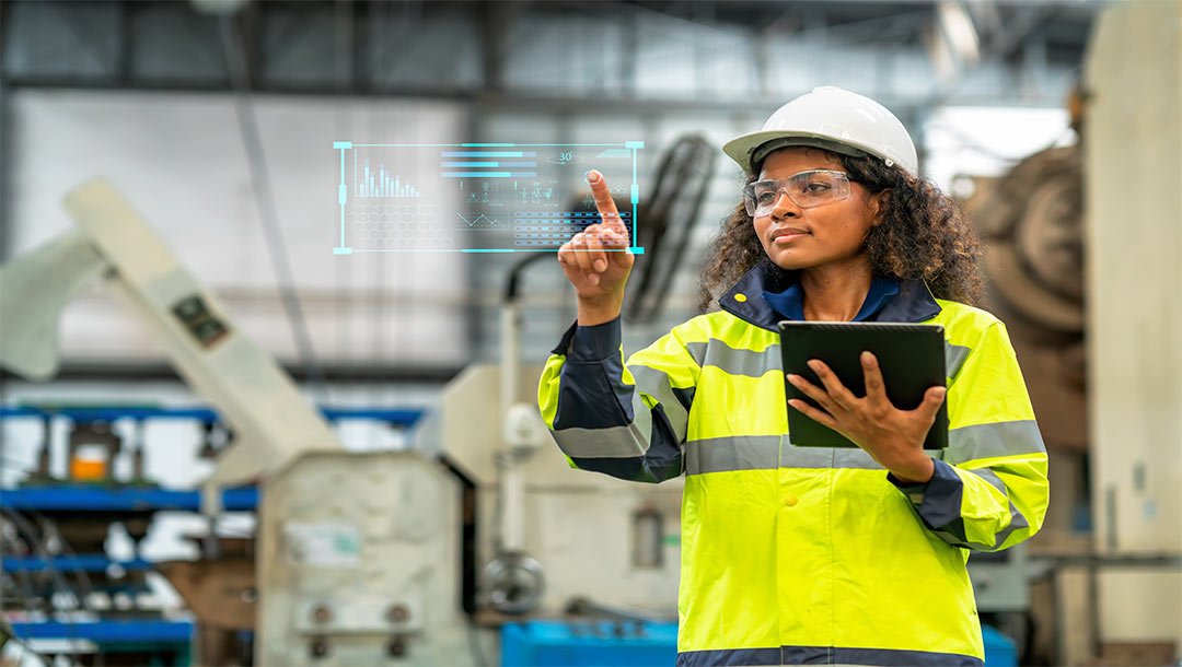 Engineer in safety gear using a tablet and interacting with a digital display in a factory