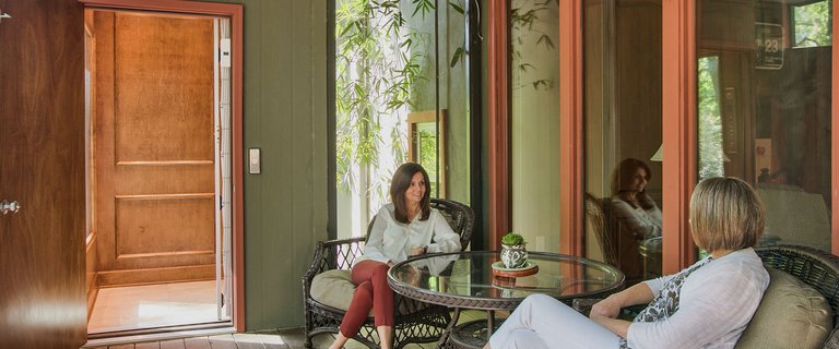 Two women sitting on a patio with an open wooden elevator door nearby