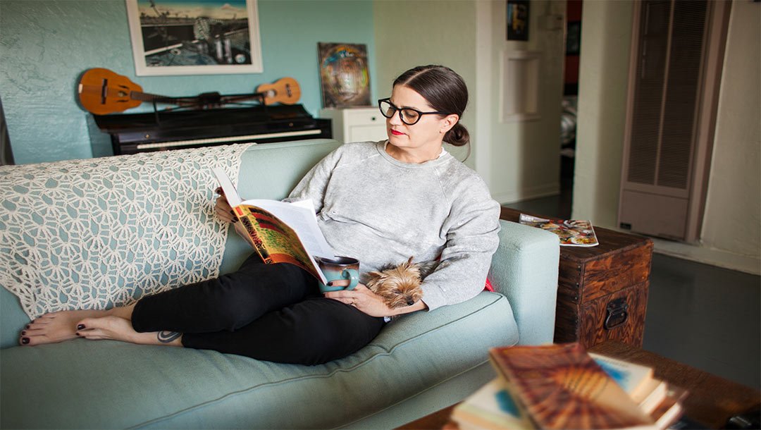 Woman sitting sofa reading book with a dog on her lap