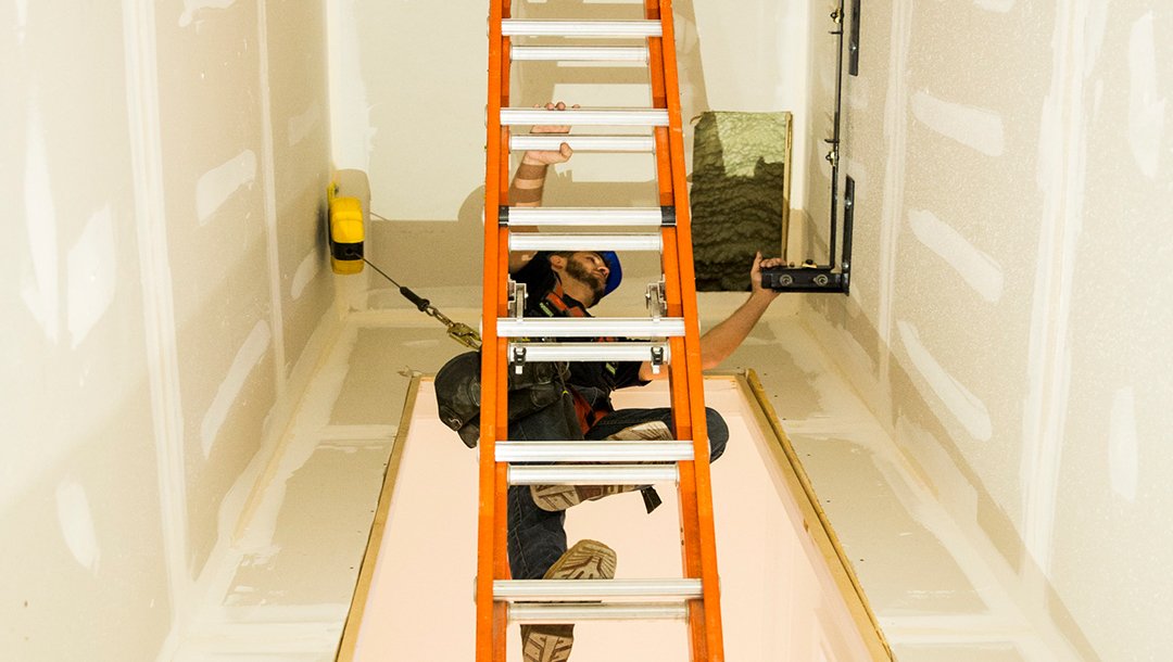 Worker on a ladder installing equipment inside an elevator shaft