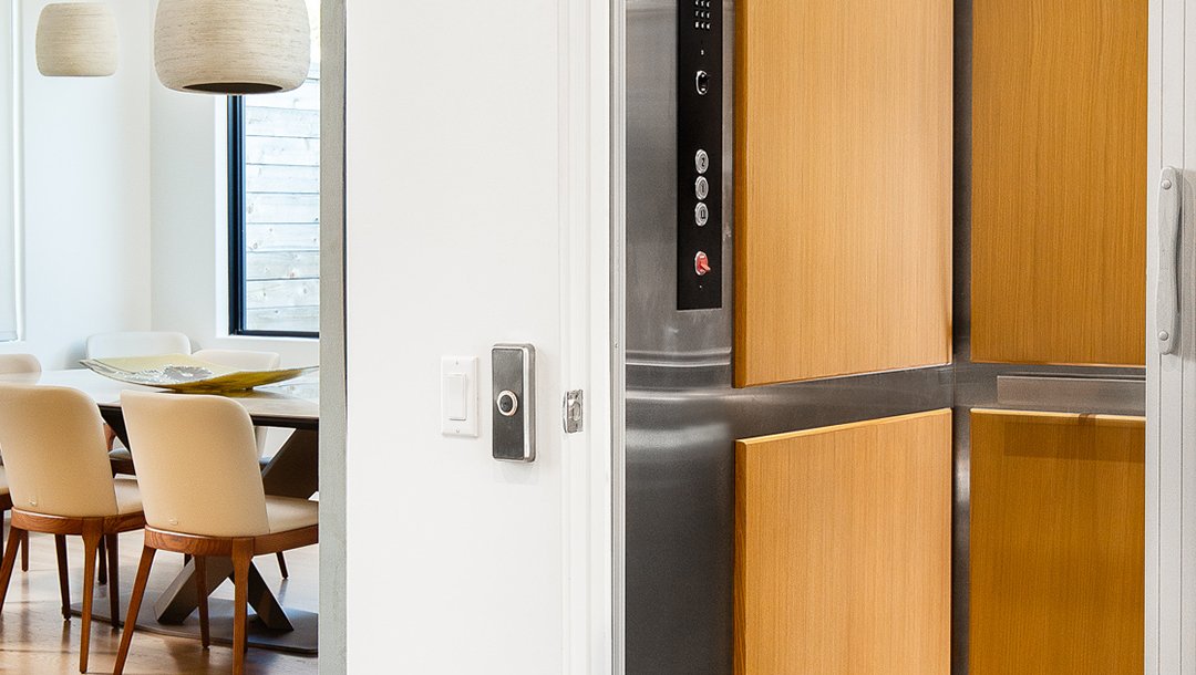 Elevator with light wood paneling next to a dining room