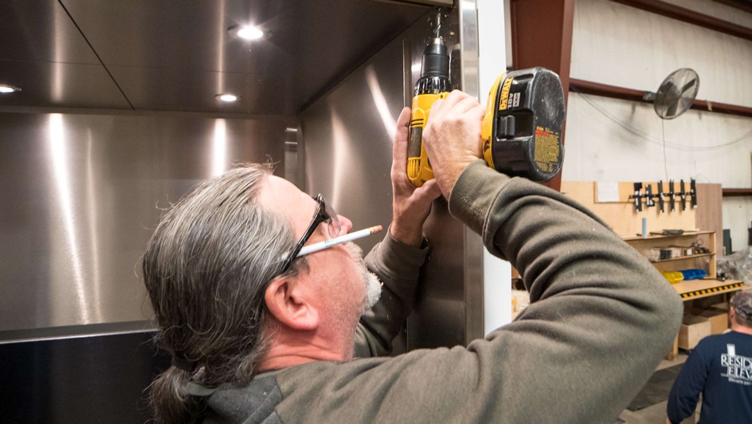 Worker using a drill to install part of a elevator