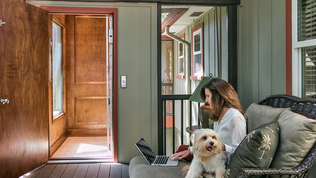Woman working on a laptop with a small dog beside her near an open home elevator