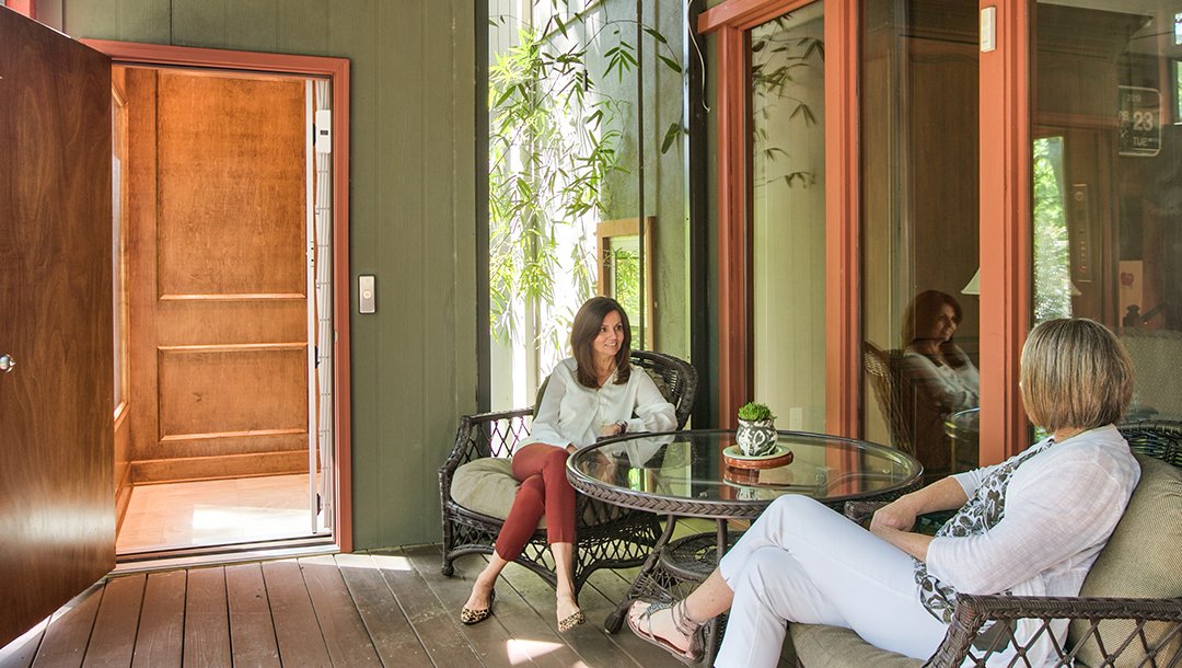 Two women sitting on a patio with an open wooden elevator door nearby