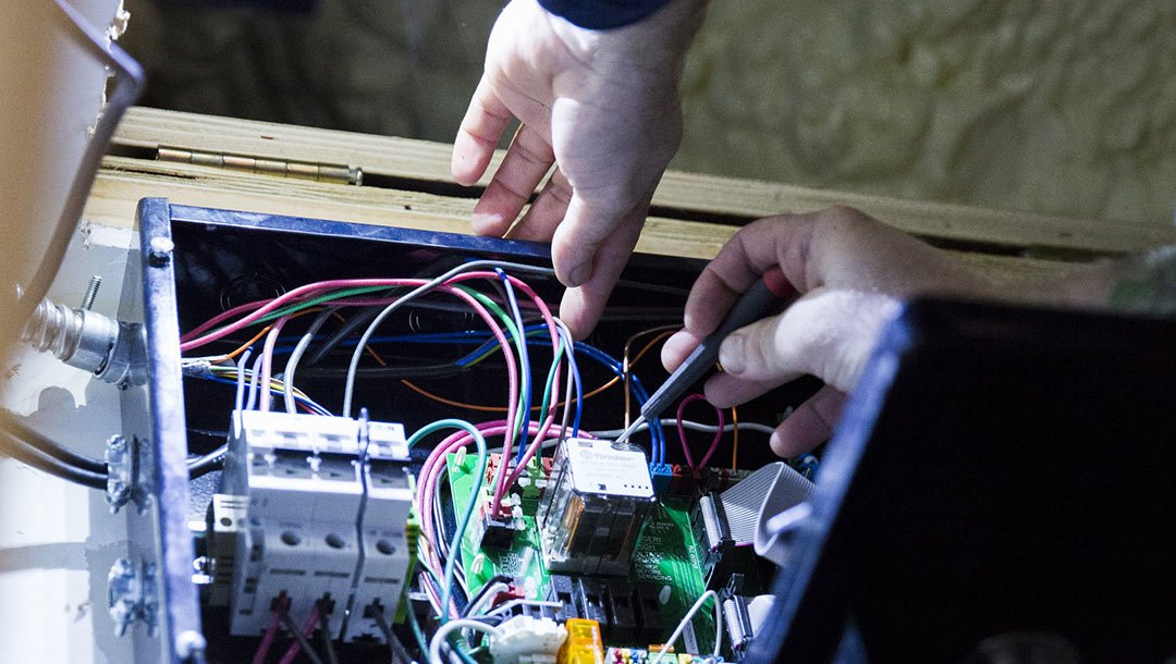 Hands working on electrical wiring inside a control panel