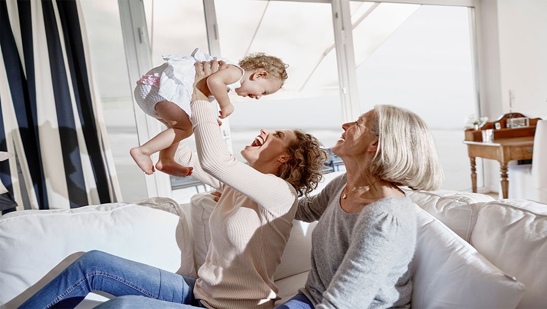 Woman lifting a laughing baby as another woman watches