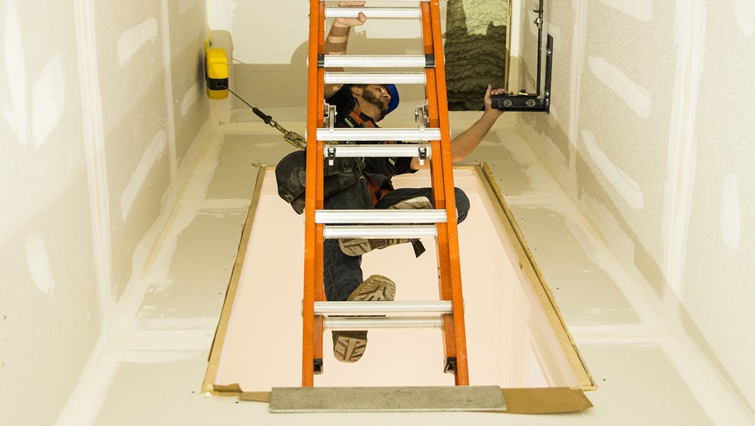 Worker on a ladder installing equipment inside an elevator shaft