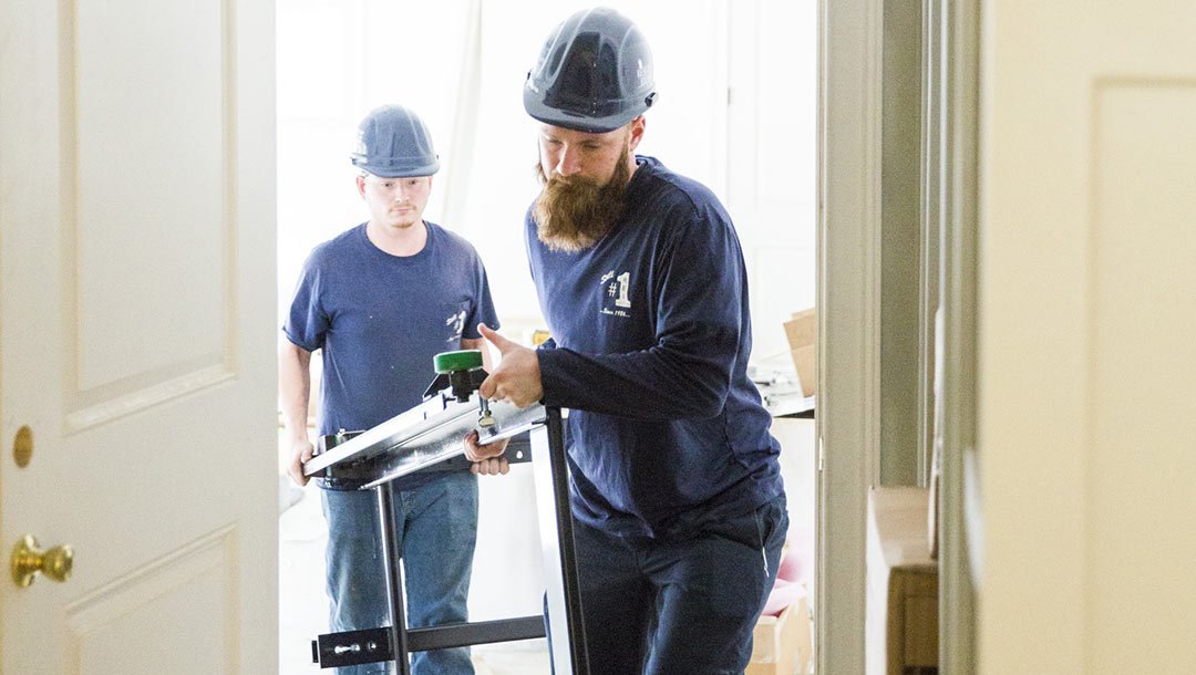 Two workers in hard hats carrying elevator components indoors