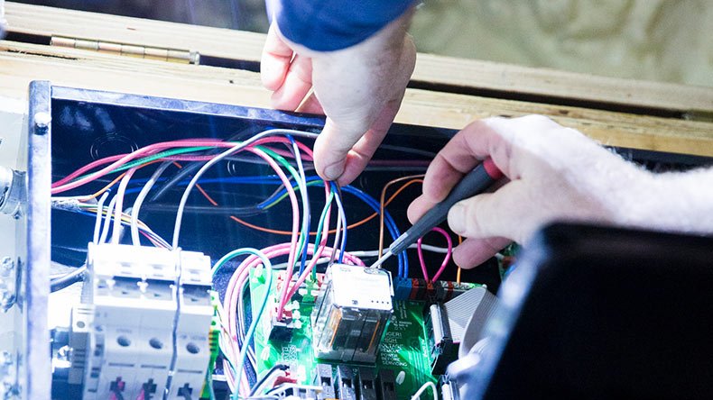Hands working on electrical wiring inside a control panel