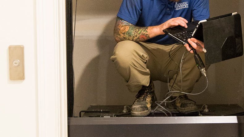 Technician crouched on equipment using a laptop for diagnostics